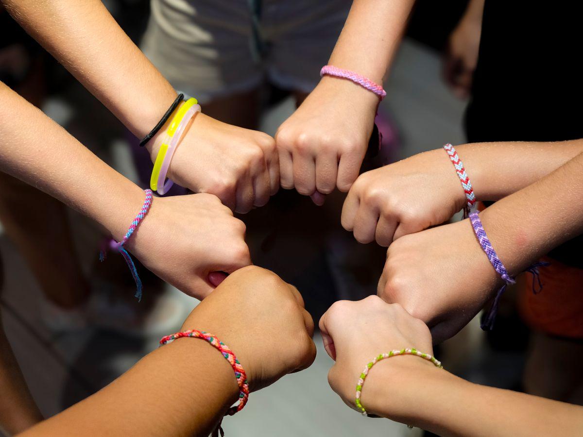A circle of hands wearing colorful friendship bracelets