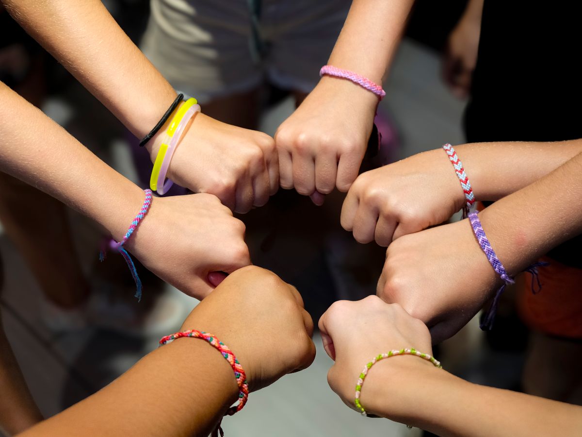 A circle of hands wearing colorful friendship bracelets